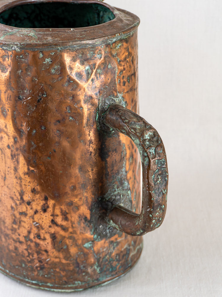 19th-century French hammered copper water carrier with handle, tarnished and aged, on a light background.