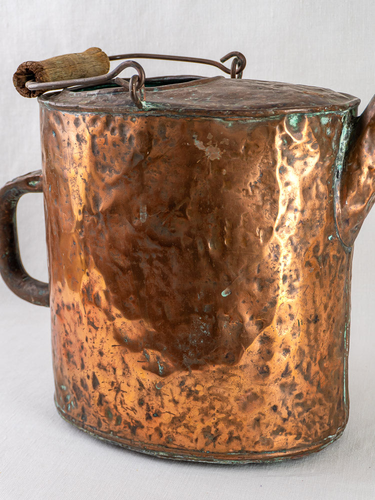 French hammered copper water carrier with visible tarnish and wooden handle, highlighting antique patina.