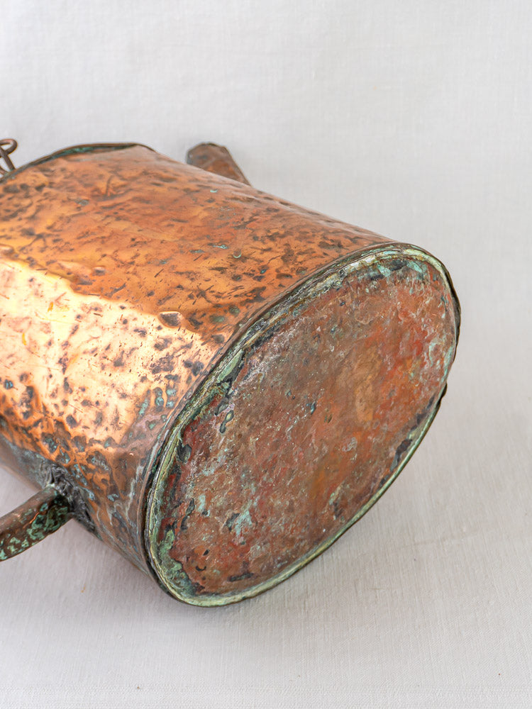 French hammered copper water carrier base with green patina and tarnish on light fabric.