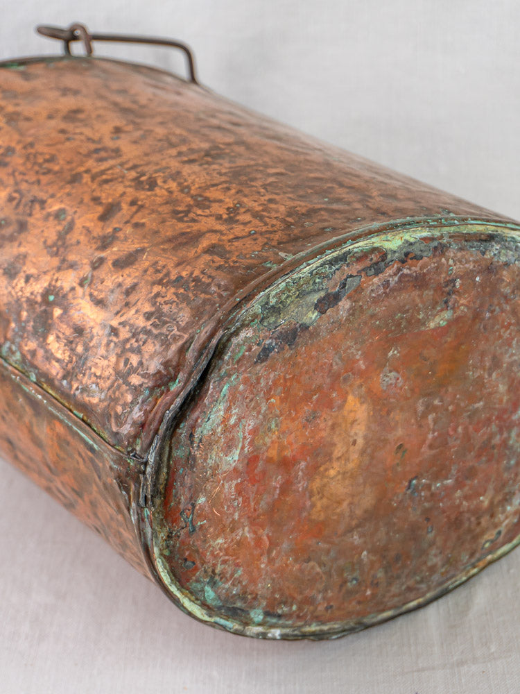 Close-up of a 19th-century French hammered copper water carrier with textured, greenish patina.