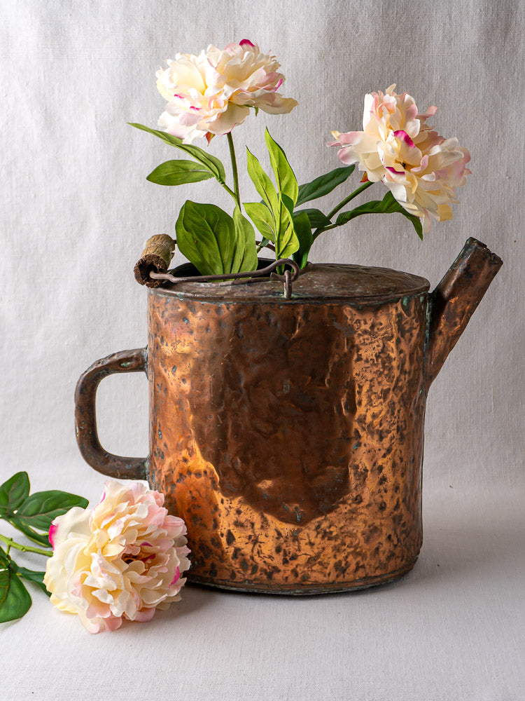 19th-century French hammered copper water carrier with pink and white peonies, on light fabric background.