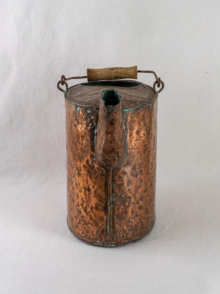 19th-century French hammered copper water carrier with cylindrical body and wooden handle on light background.