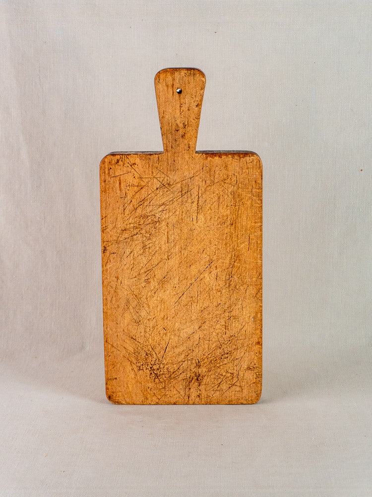 Antique French rectangular paddle handle cutting board with knife marks, upright against a light background.