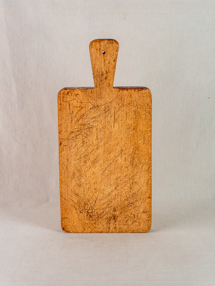 Antique French rectangular paddle handle cutting board with knife marks, upright against a light background.