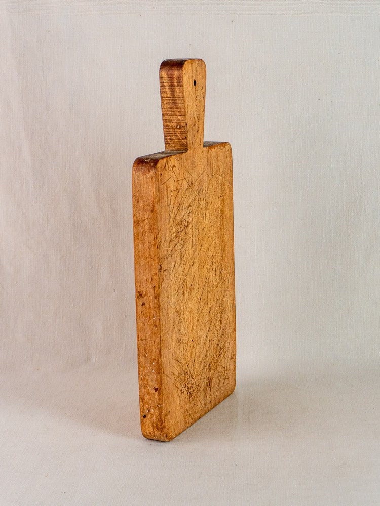 Antique French paddle handle cutting board with subtle wear, upright on a light surface.