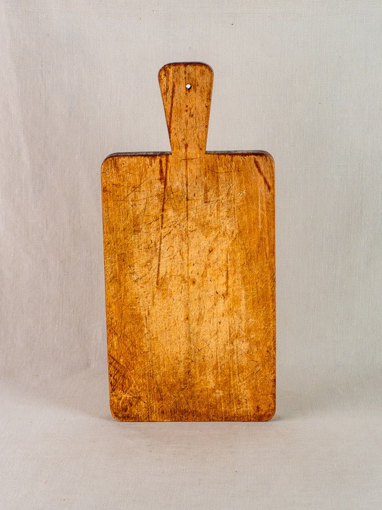 Antique French paddle handle cutting board with cut marks and aged wood set against a light background.