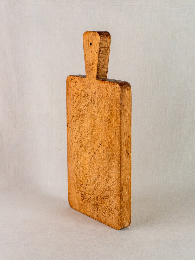 Antique French paddle handle cutting board with knife marks, upright on a neutral surface.