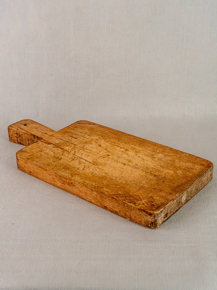 Antique French paddle handle cutting board with visible wear, resting on a light fabric surface.
