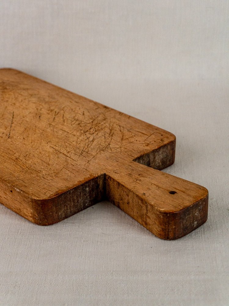 Antique French paddle handle cutting board, late 19th century, well-worn surface with knife marks on light fabric.