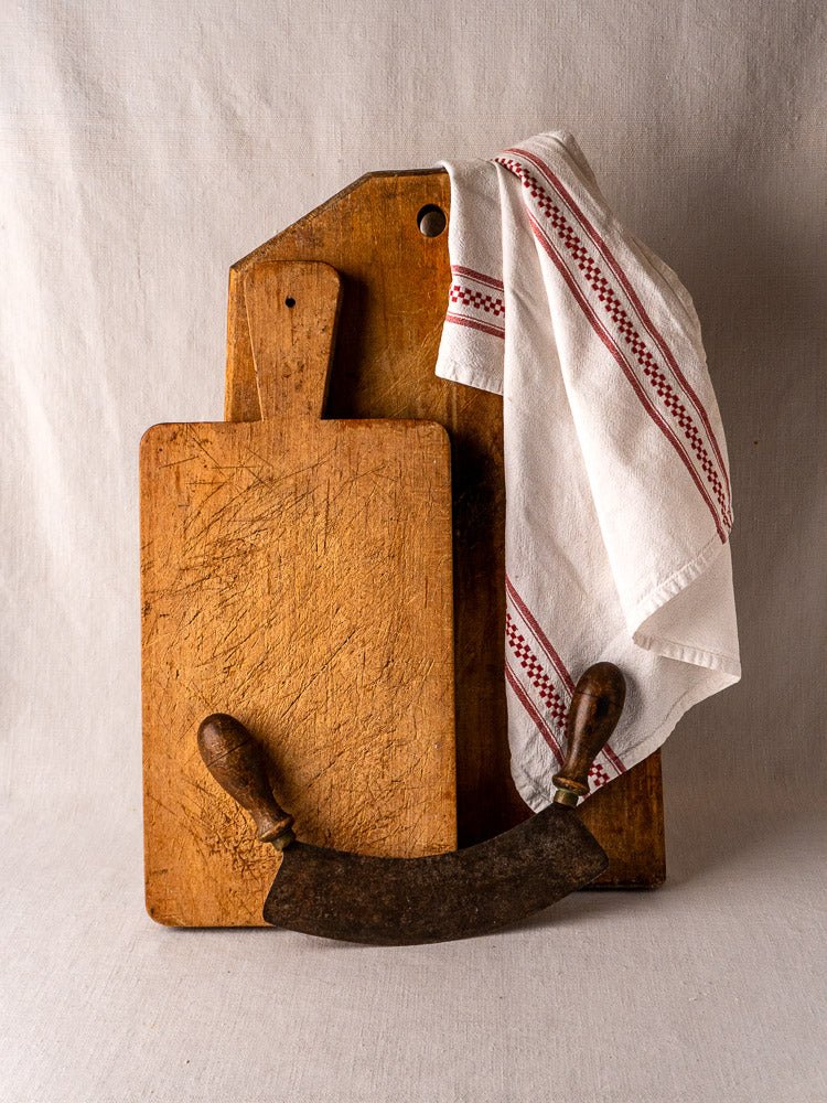 Antique French paddle handle cutting board with striped linen and vintage curved metal herb chopper.