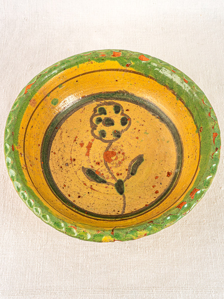 Antique 18th-century French slipware bowl with green rim, yellow interior, and hand-painted black flower.