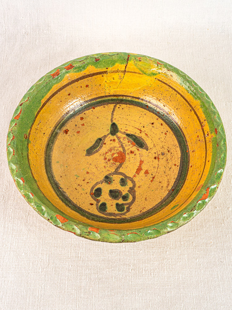 18th century French slipware bowl, hand-painted floral motif, vibrant glaze, on light fabric background.