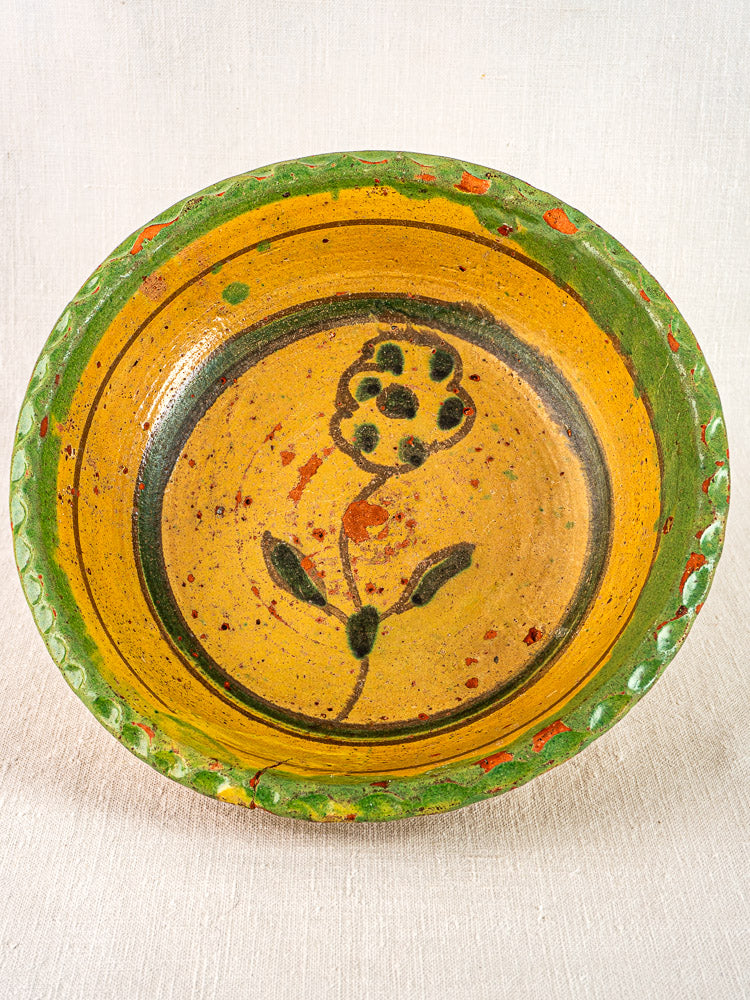 18th-century French slipware bowl with yellow glaze, green rim, and central black floral motif.