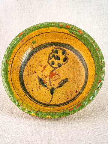 18th-century French slipware bowl with yellow glaze, green rim, and central black floral motif.
