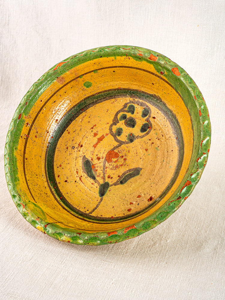Antique 18th-century French yellow slipware bowl with green rim and black floral center motif.
