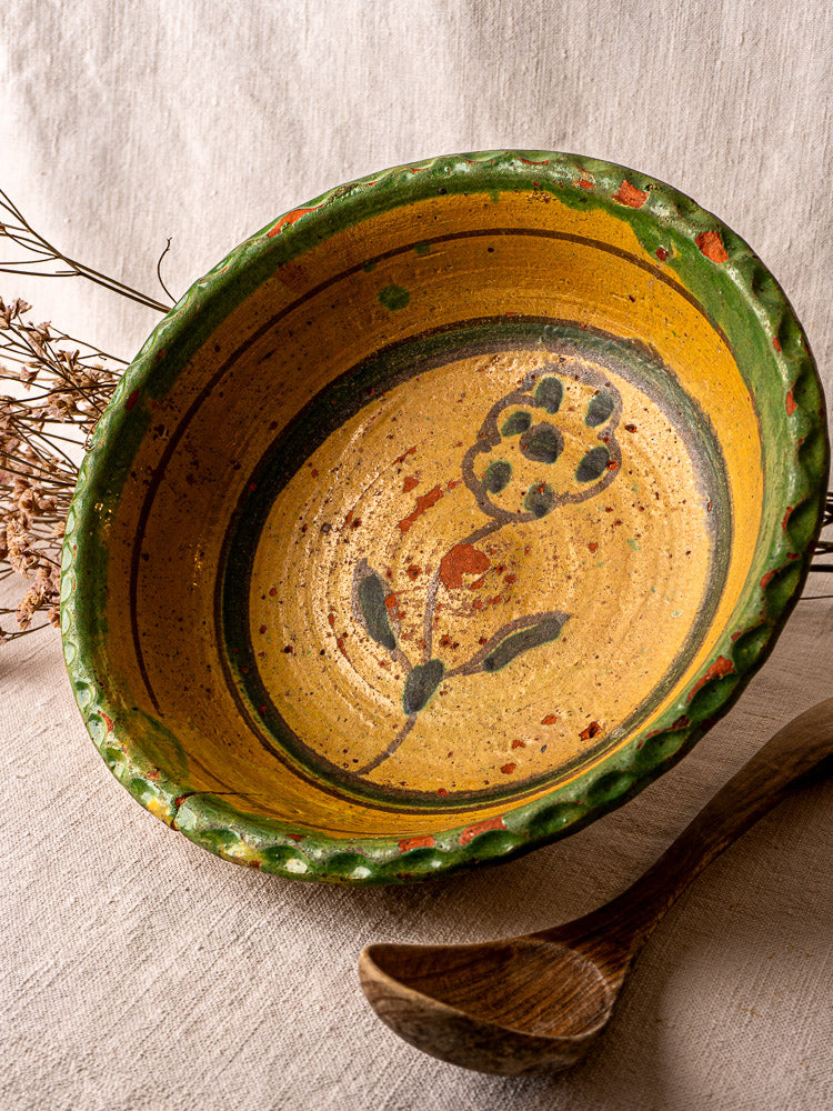 18th-century French slipware bowl with yellow glaze, green rim, and central black floral motif.