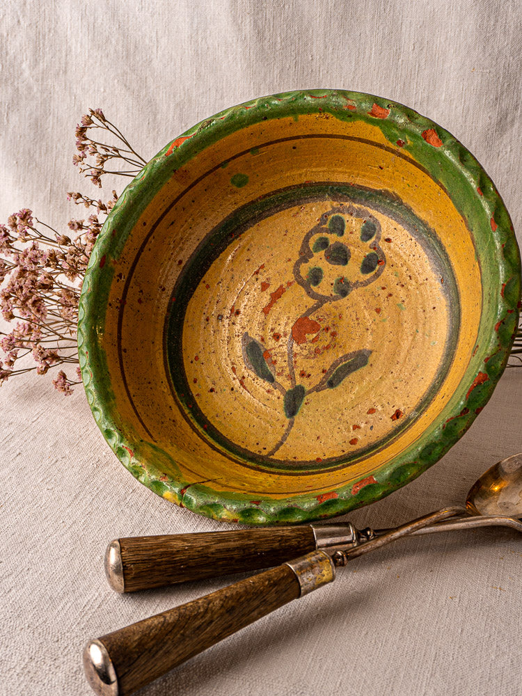 18th-century French slipware bowl, hand painted with flowers and a green rim, on linen with dried flowers.