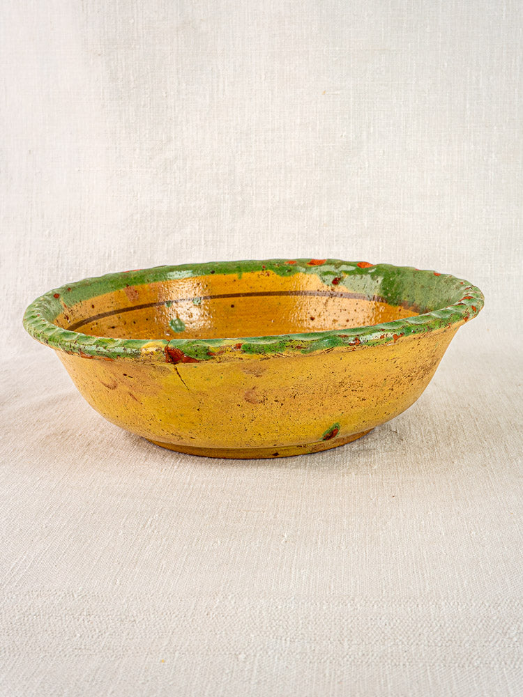 18th-century French slipware bowl with hand-painted floral motifs, rustic yellow glaze, and green trim.