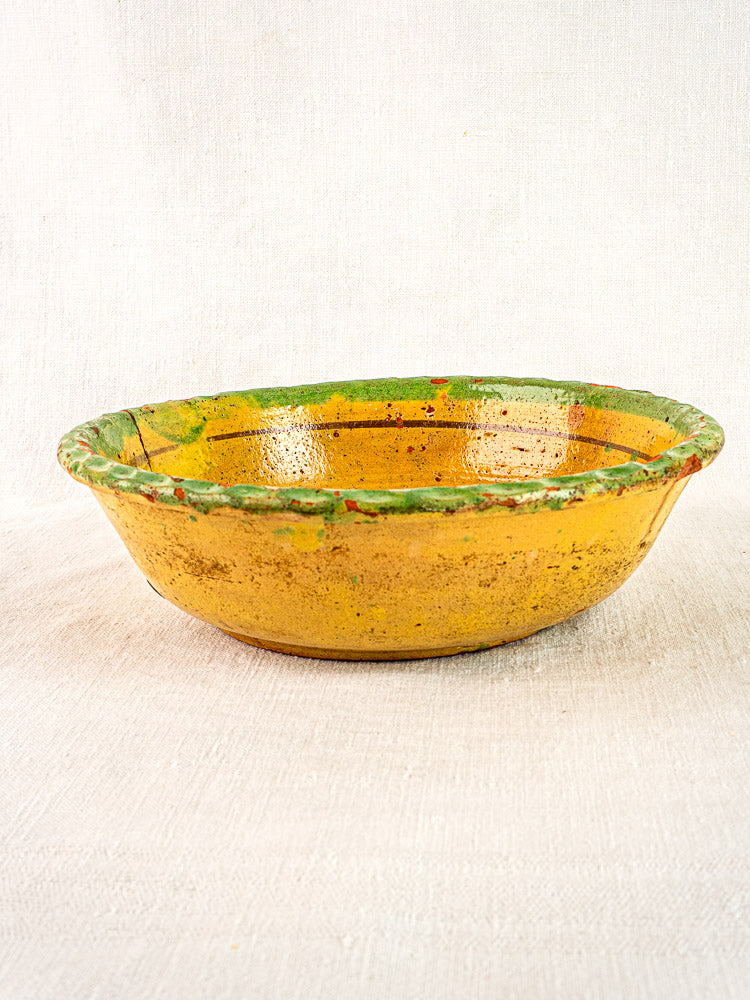 18th-century French slipware bowl with yellow glaze, green rim, and floral motif on light textured surface.