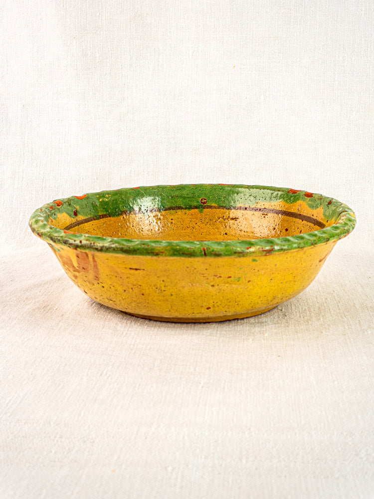 18th-century French slipware bowl with hand-painted florals, yellow base, green rim, on light fabric.