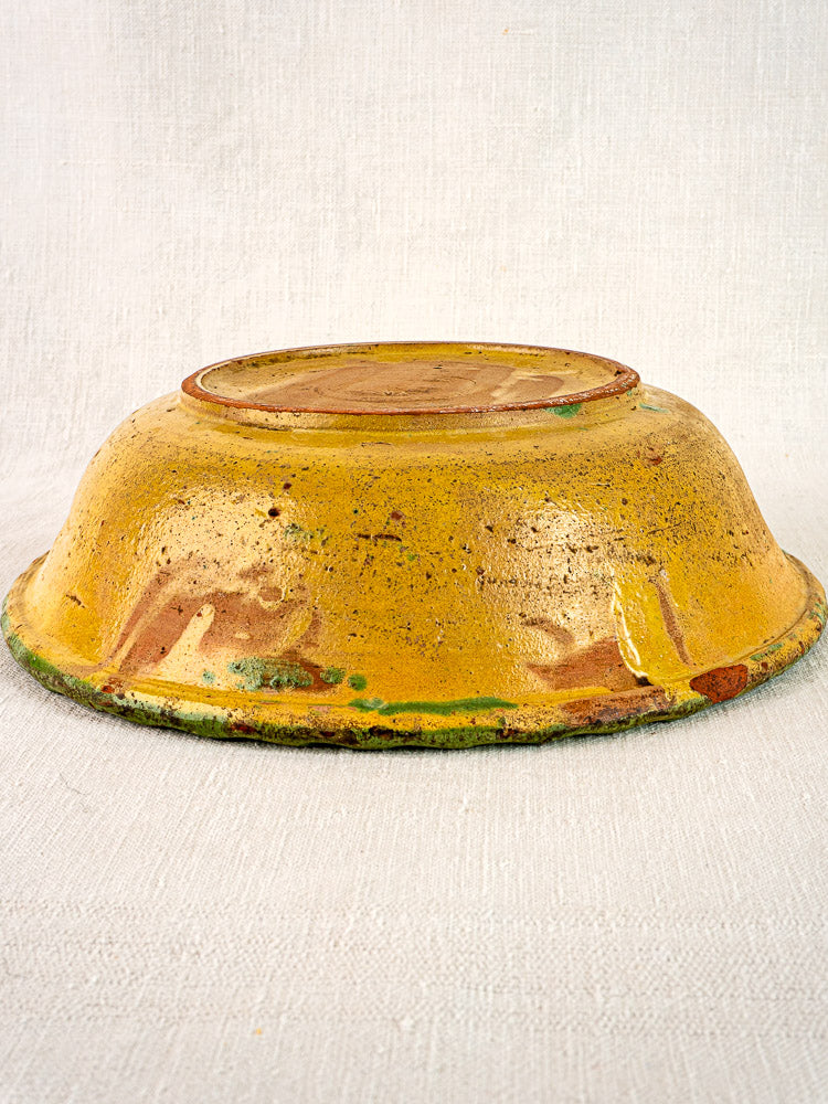 18th century French slipware bowl with rustic yellow glaze, brown and green floral accents on off-white fabric.