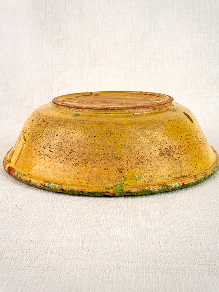 18th-century French slipware bowl with hand painted floral motifs, yellowish-gold glaze, and aged patina on fabric.