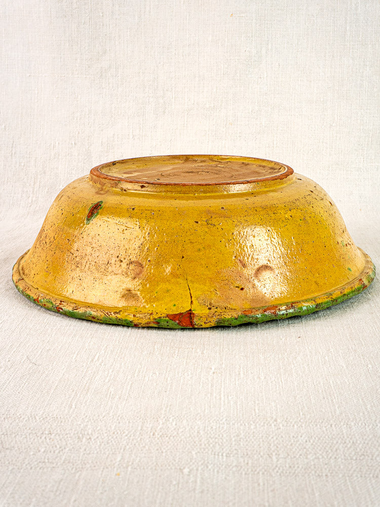 18th-century French slipware bowl, upside down on neutral fabric, showing worn, hand-painted floral base.