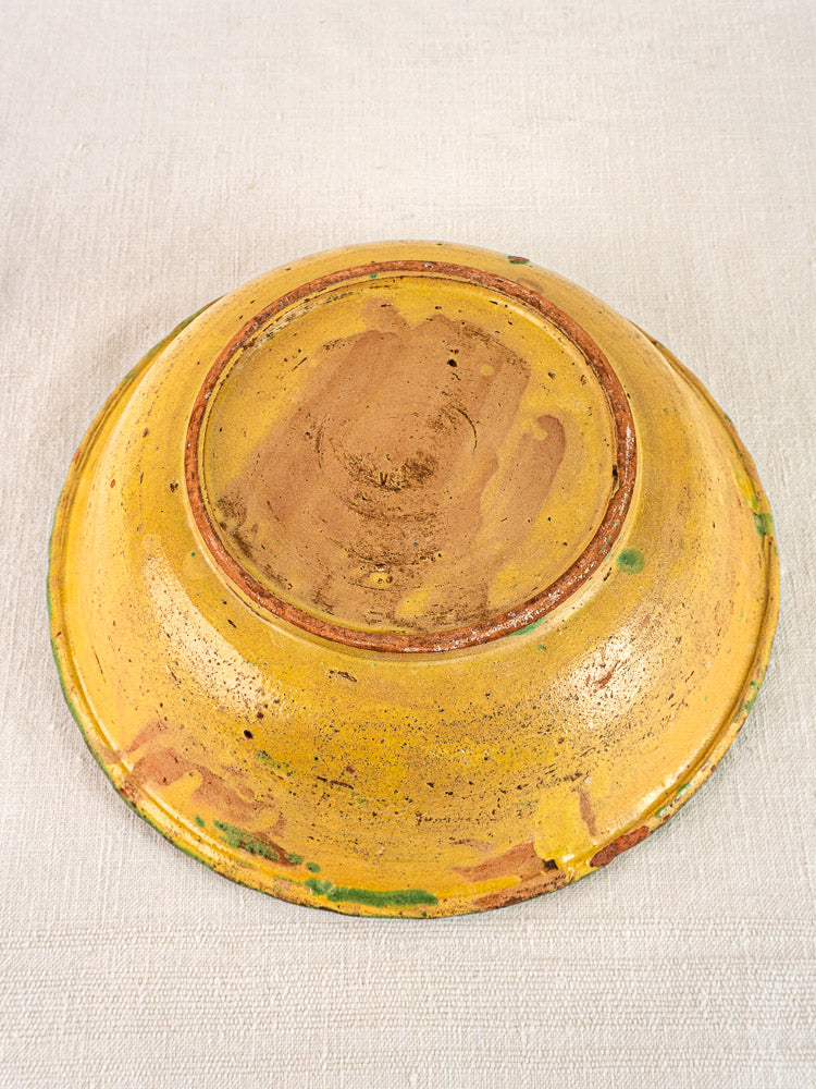 Antique French 18th-century slipware bowl with floral motif, yellow-green glaze, upside down on beige textured surface.