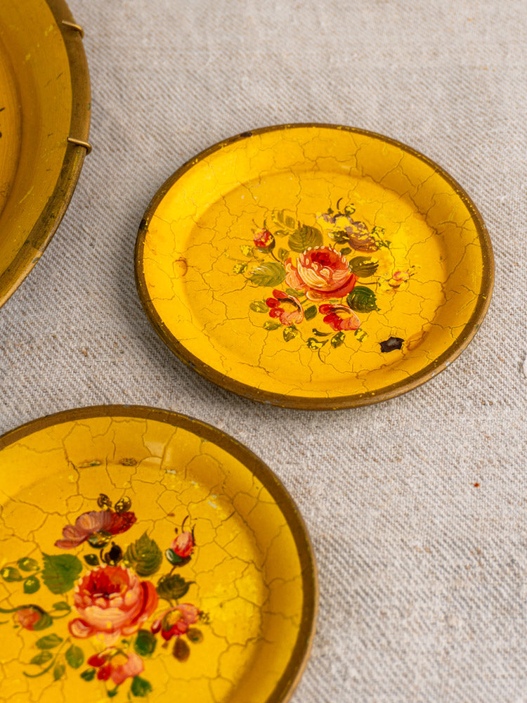 Pair of small round yellow French tole trays with floral motifs and age-related cracks on beige fabric.