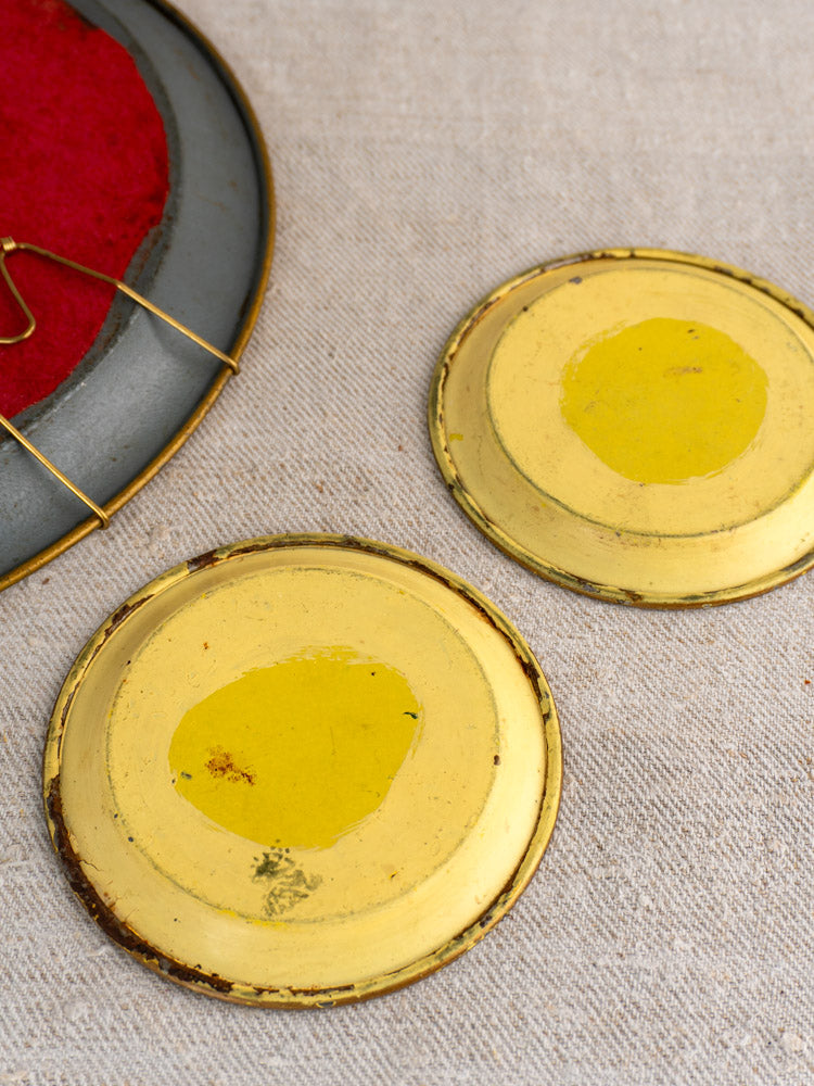 Two round yellow-gold metal lids with yellow centers on beige fabric; Antique French Tole Tray Set partially visible.