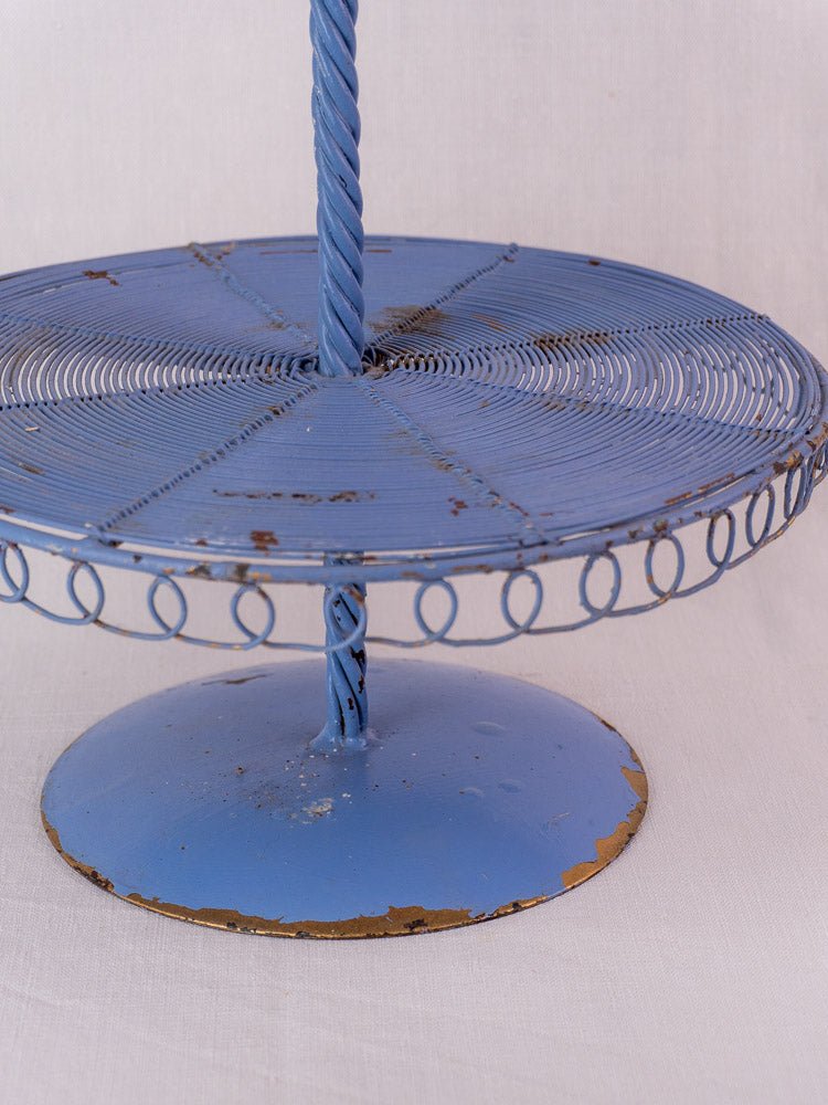 Blue antique French three-tier wire pastry stand with circular patterns and distressed paint on white fabric.