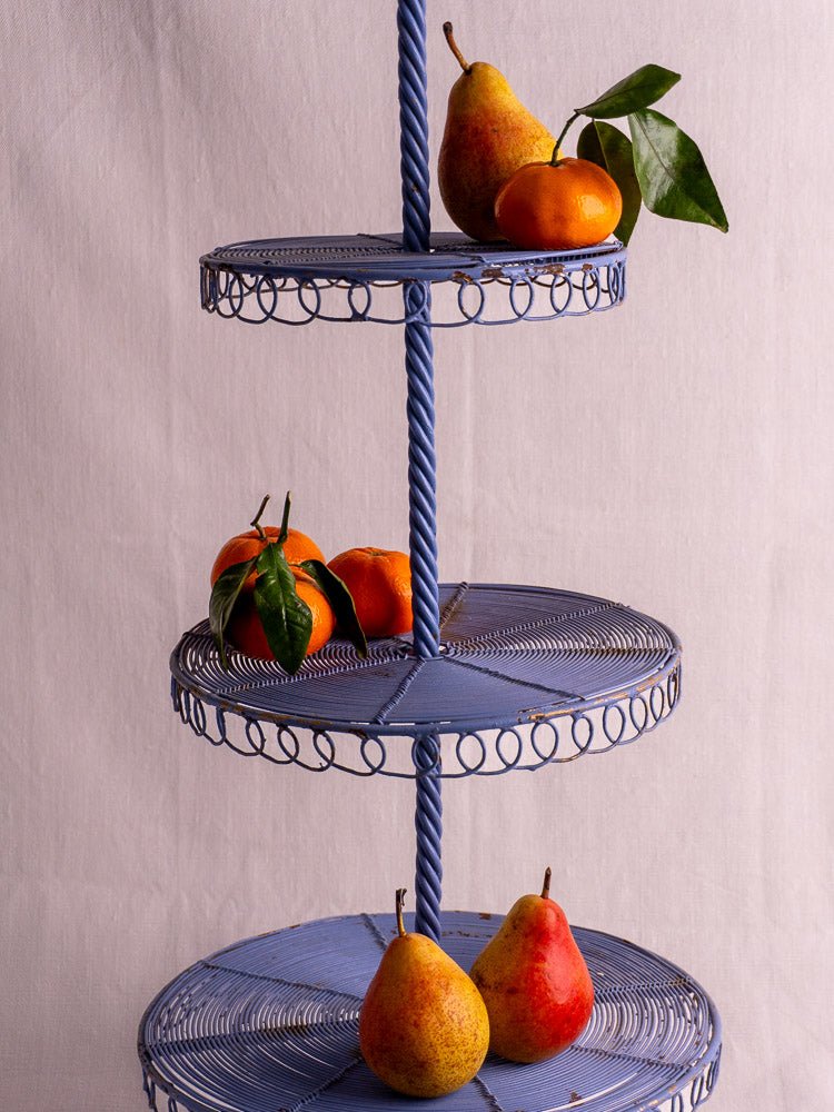 Antique French blue three-tier wirework pastry stand with pears, tangerines, and leaves on beige background.