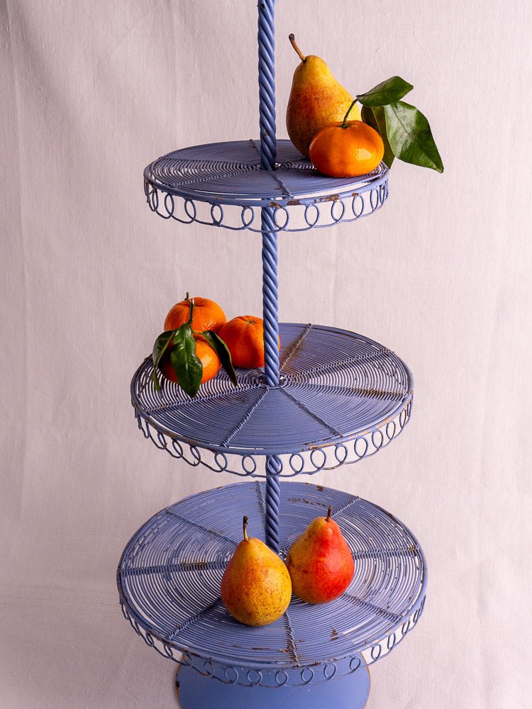 Antique French blue three-tier wirework pâtisserie stand holding pears and oranges with green leaves.