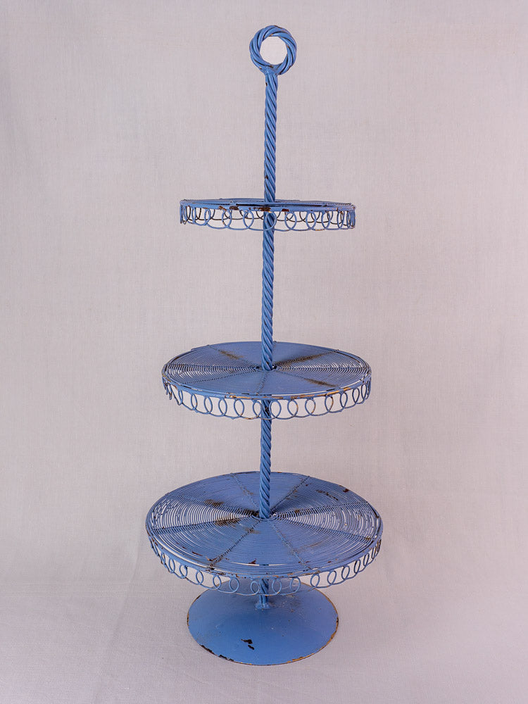 Antique French blue three-tier wire pastry stand with circular trays and twisted central rod on a light background.
