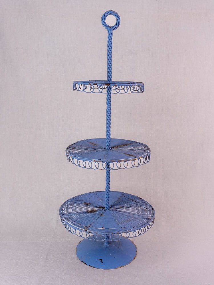 Antique French blue three-tier wire pastry stand with circular trays and twisted central rod on a light background.
