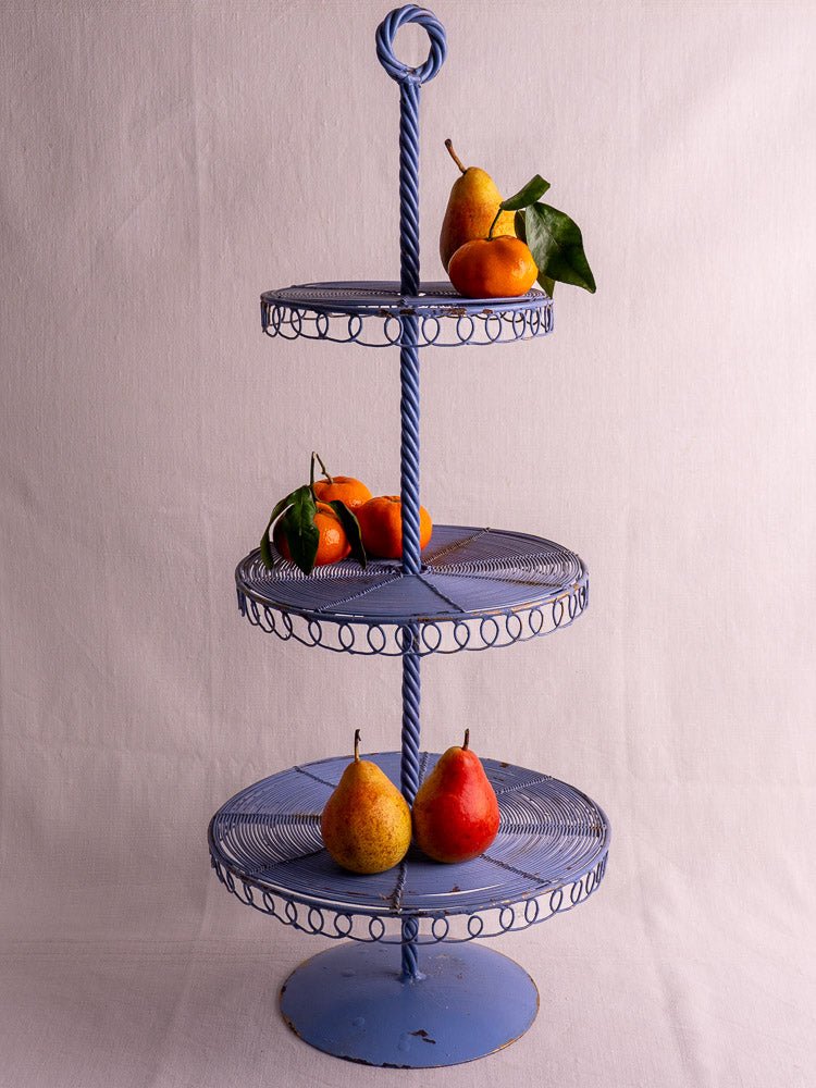 Antique French blue three-tier wirework pastry stand with pears and tangerines, pale backdrop.