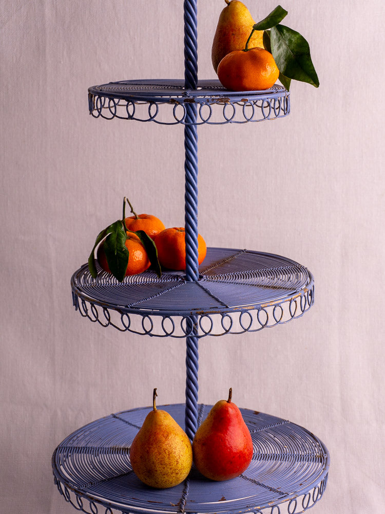 Antique French blue three-tier wire pastry stand with circular trays and twisted central rod on a light background.