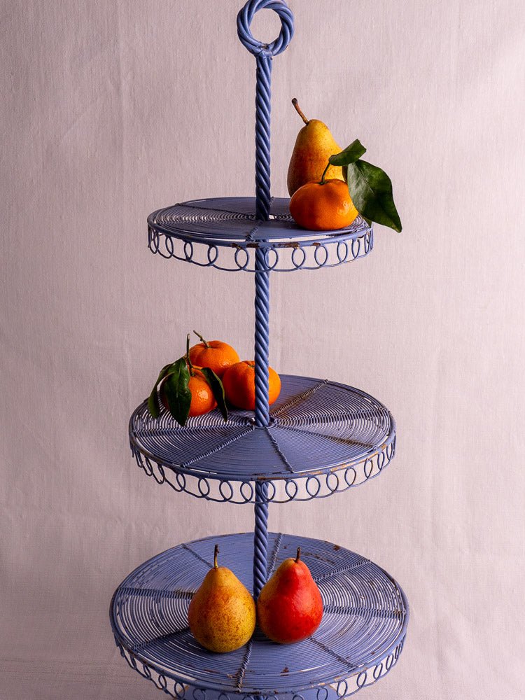 Blue three-tier antique French wire pâtisserie stand with pears and oranges, light background.