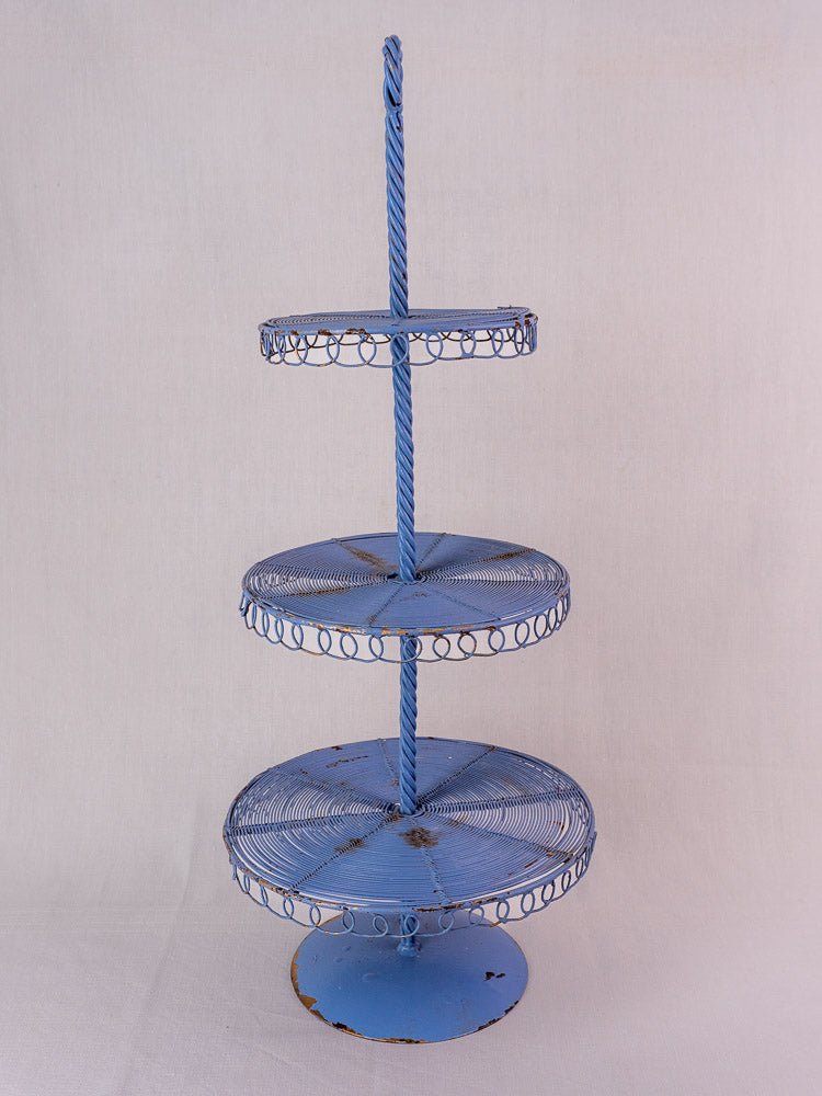Antique French blue metal three-tier wirework pâtisserie stand with ornate edging, on white background.
