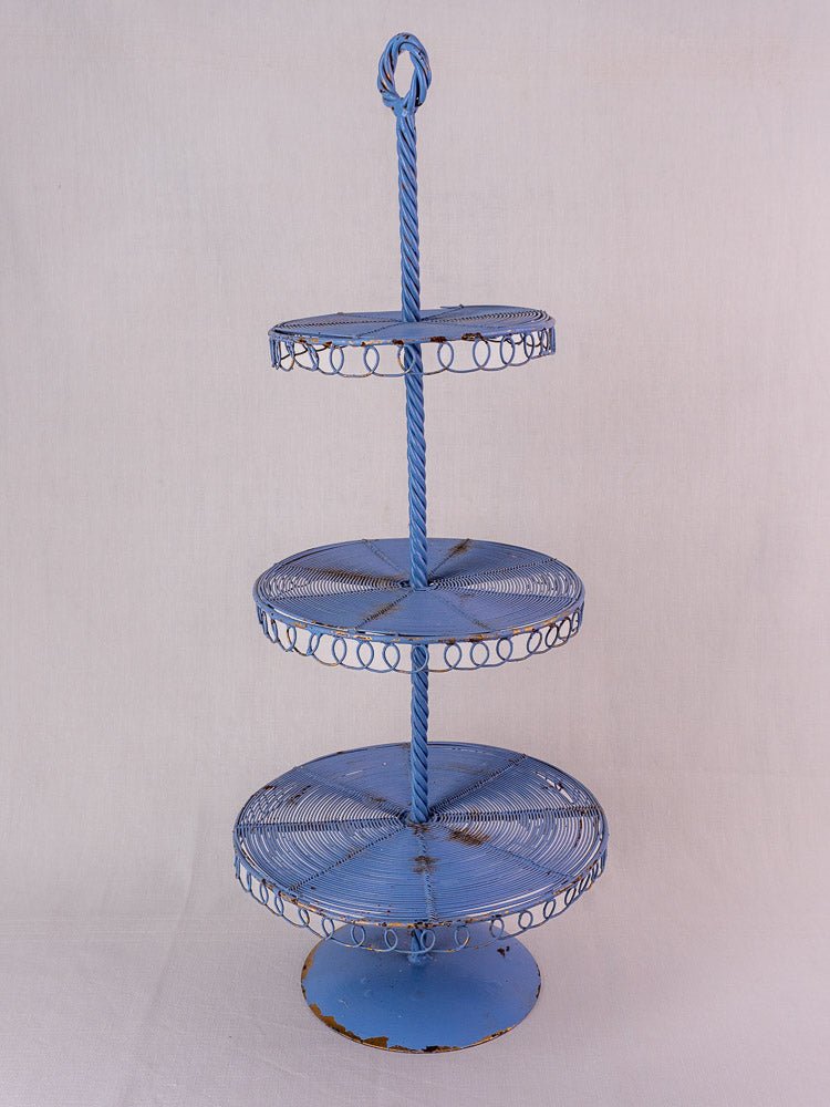 Antique French blue three-tier wirework pastry stand with circular trays and twisted top handle, on light background.