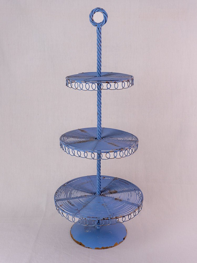 Antique French blue three-tier wirework pastry stand with loop handle and distressed finish on white background.