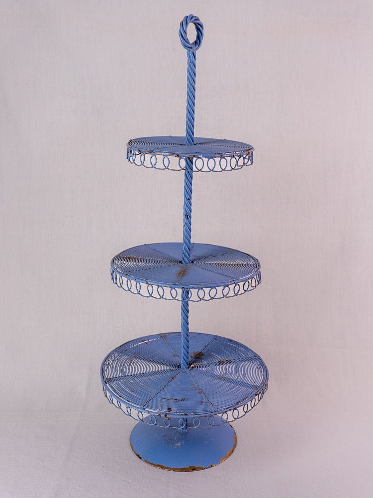Antique French blue three-tier wirework pastry stand with ornate edge loops and central twisted rod, vintage wear and base rust.