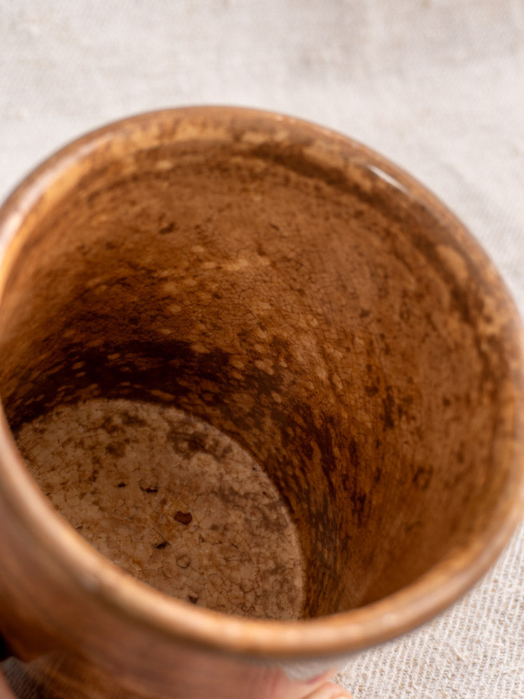 Interior detail of antique French Pot à Confiture by Creil et Montereau with mottled brown glaze, on light fabric.