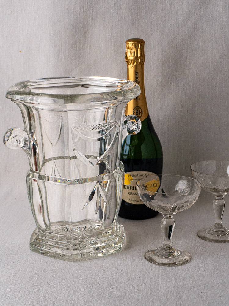 French cut crystal champagne bucket with champagne bottle and coupe glasses on light fabric background.