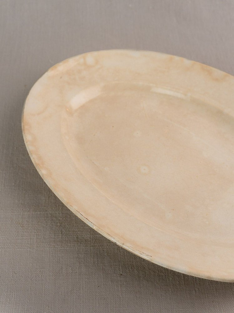Vintage French Sarreguemines ivory ironstone platter by Digoin with stains and wear on gray surface.