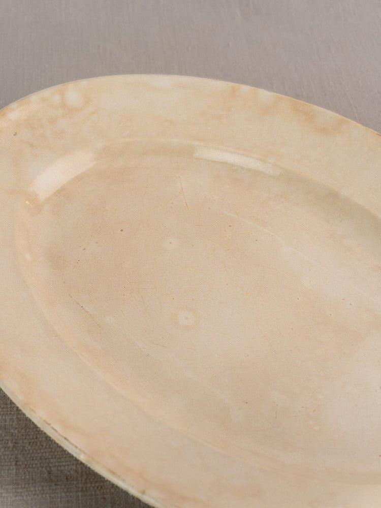 Vintage French Sarreguemines oval ivory ironstone platter by Digoin, cracks and stains, on neutral fabric.
