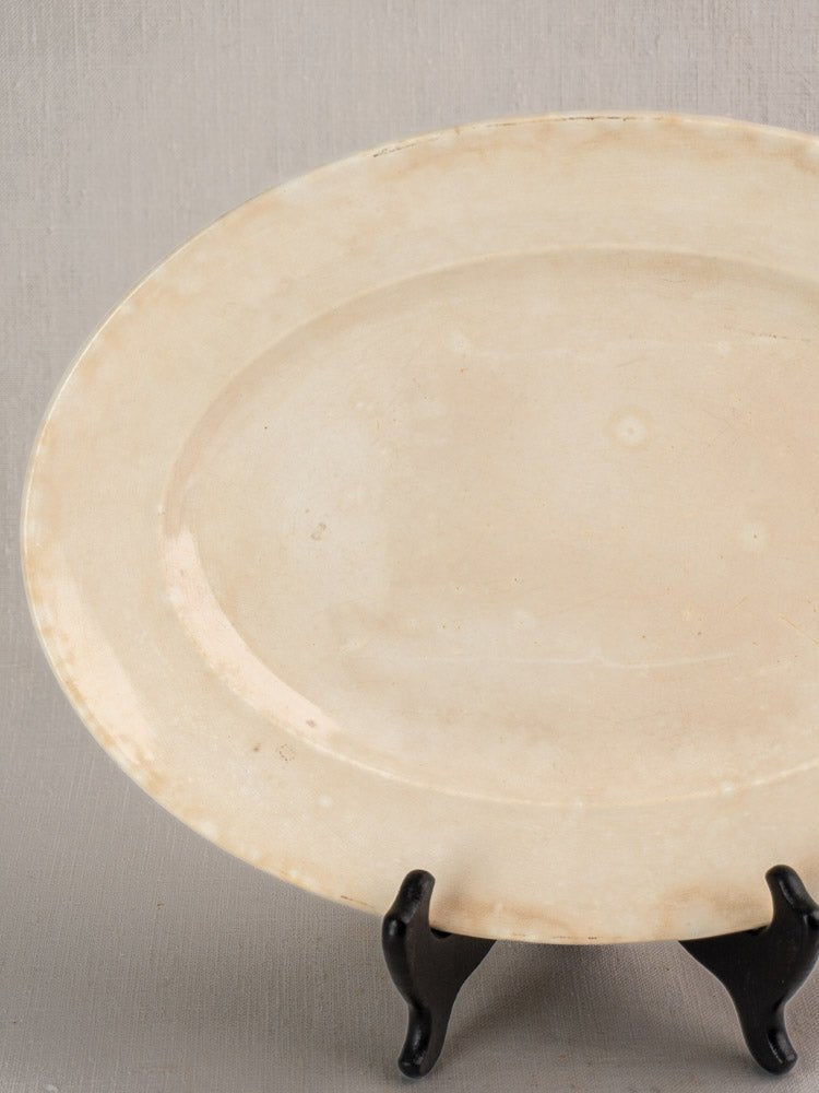 Vintage French Sarreguemines ivory ironstone platter, oval and plain, on black stand, neutral background.