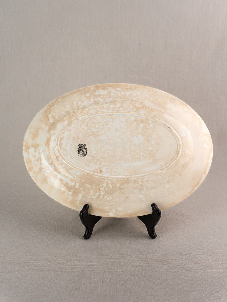 Oval vintage French Sarreguemines ivory ironstone platter with mottled beige-white glaze, shown on black stand.