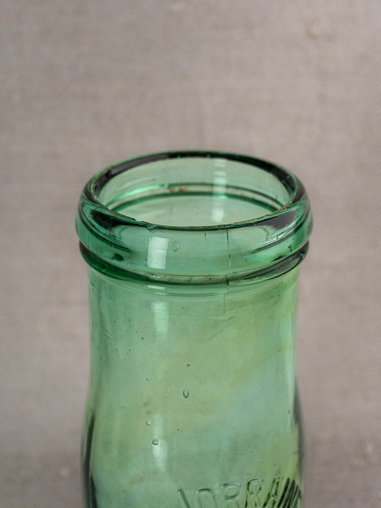 Thick rim of Antique French La Lorraine green glass jar with thistle motif, early-mid 20th century, on neutral background.