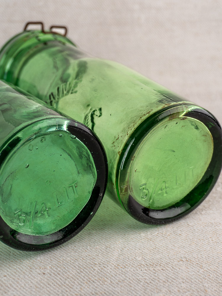 Pair of Antique French La Lorraine green glass jars with thistle motif and “3/4 LIT.” embossed bases on beige cloth.